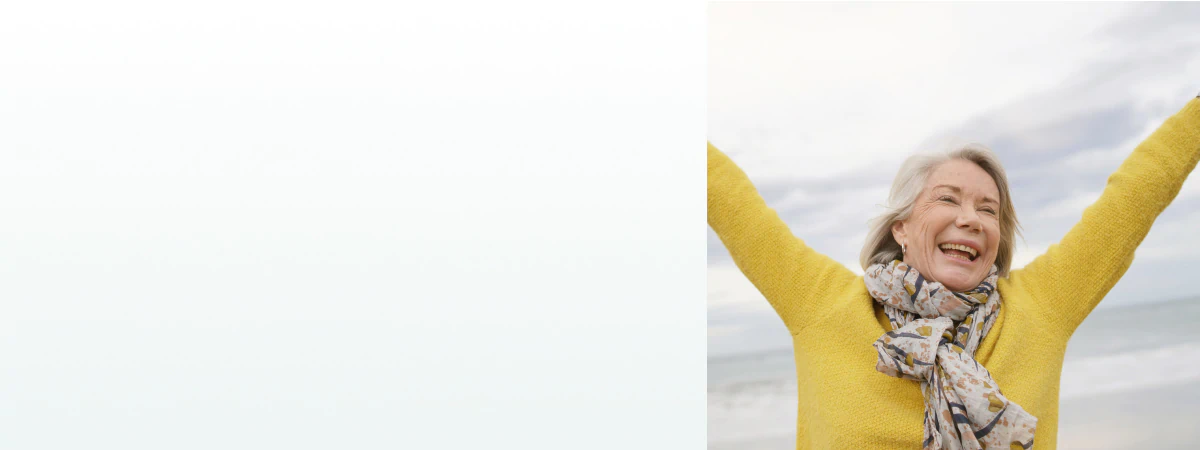 A joyful elderly woman raising her arms at the beach, representing the benefits of supplements for energy and vitality.