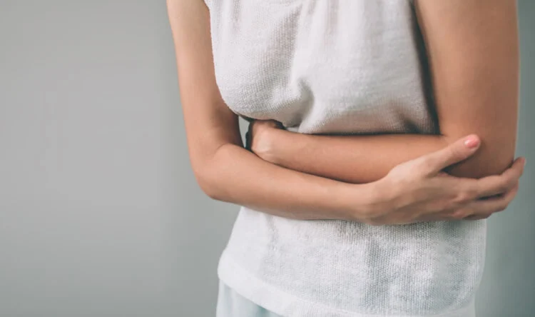 A woman clutching her stomach in discomfort, representing the need for supplements for gut health and digestion.