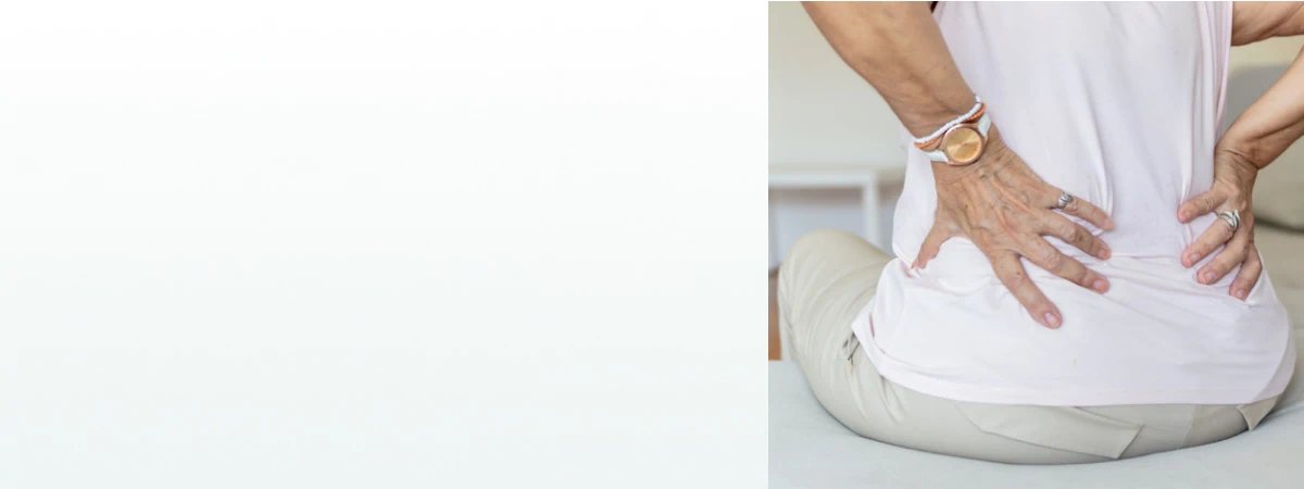 A woman sitting on a couch holding her lower back, representing the need for supplements for kidney health.